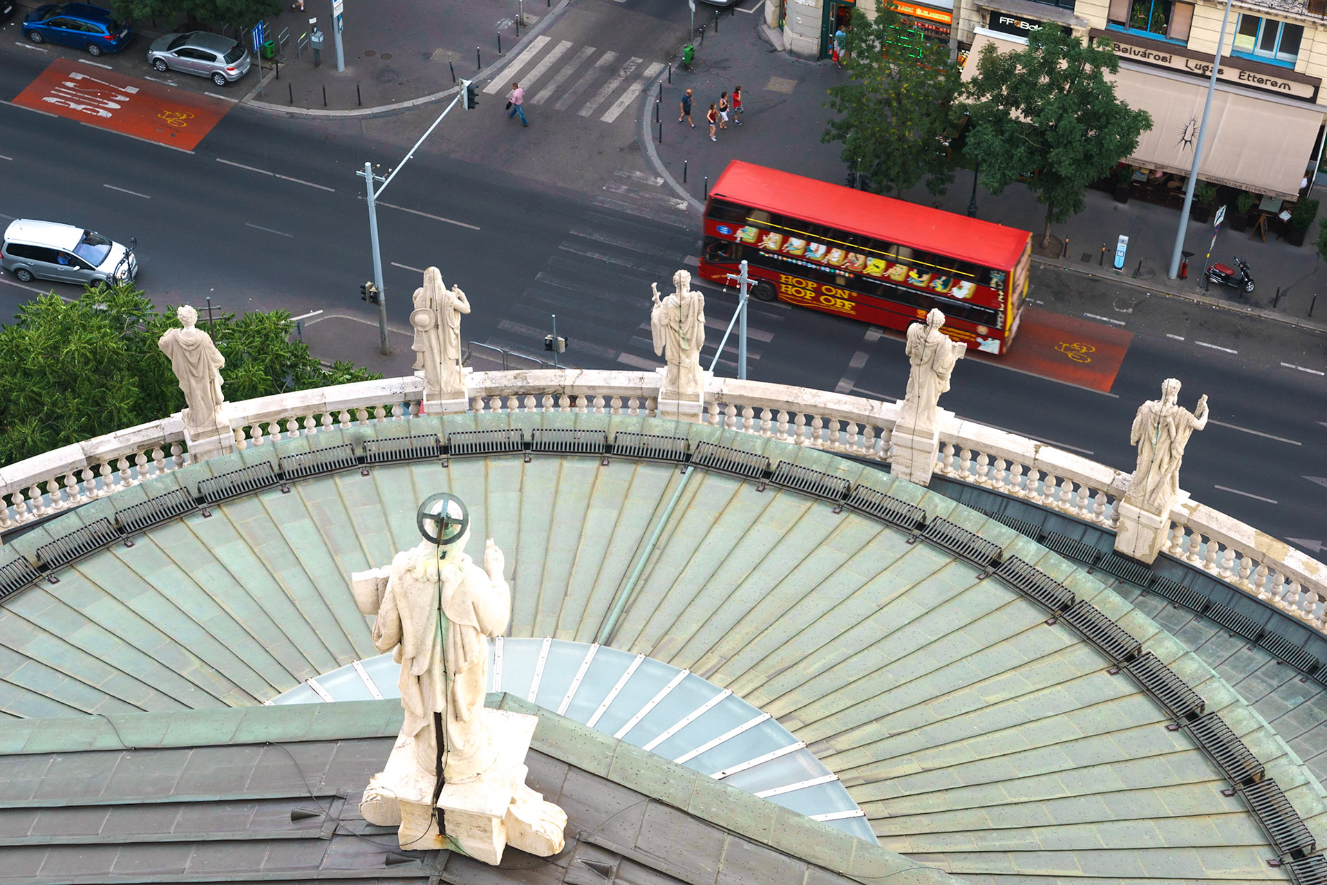 Szent István-bazilika'nın çatısından görülebilen heykeller, yoldan geçen bir turist otobüsünü selamlar gibi görünüyor.