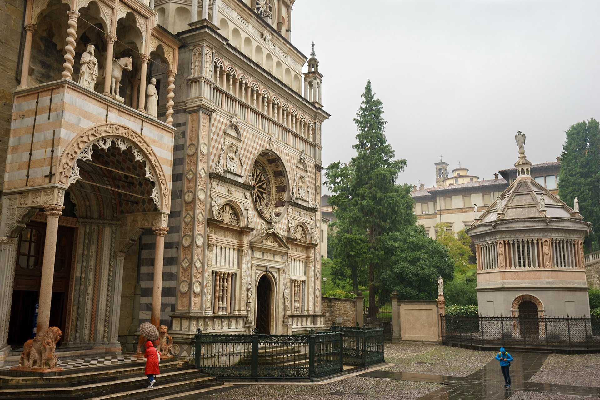 Sağanak yağmur altında, Bergamo Piskoposluğu Tarihi Arşivi'nin önündeki iki turist, yağmurlukları ile kadraja renk katıyor.