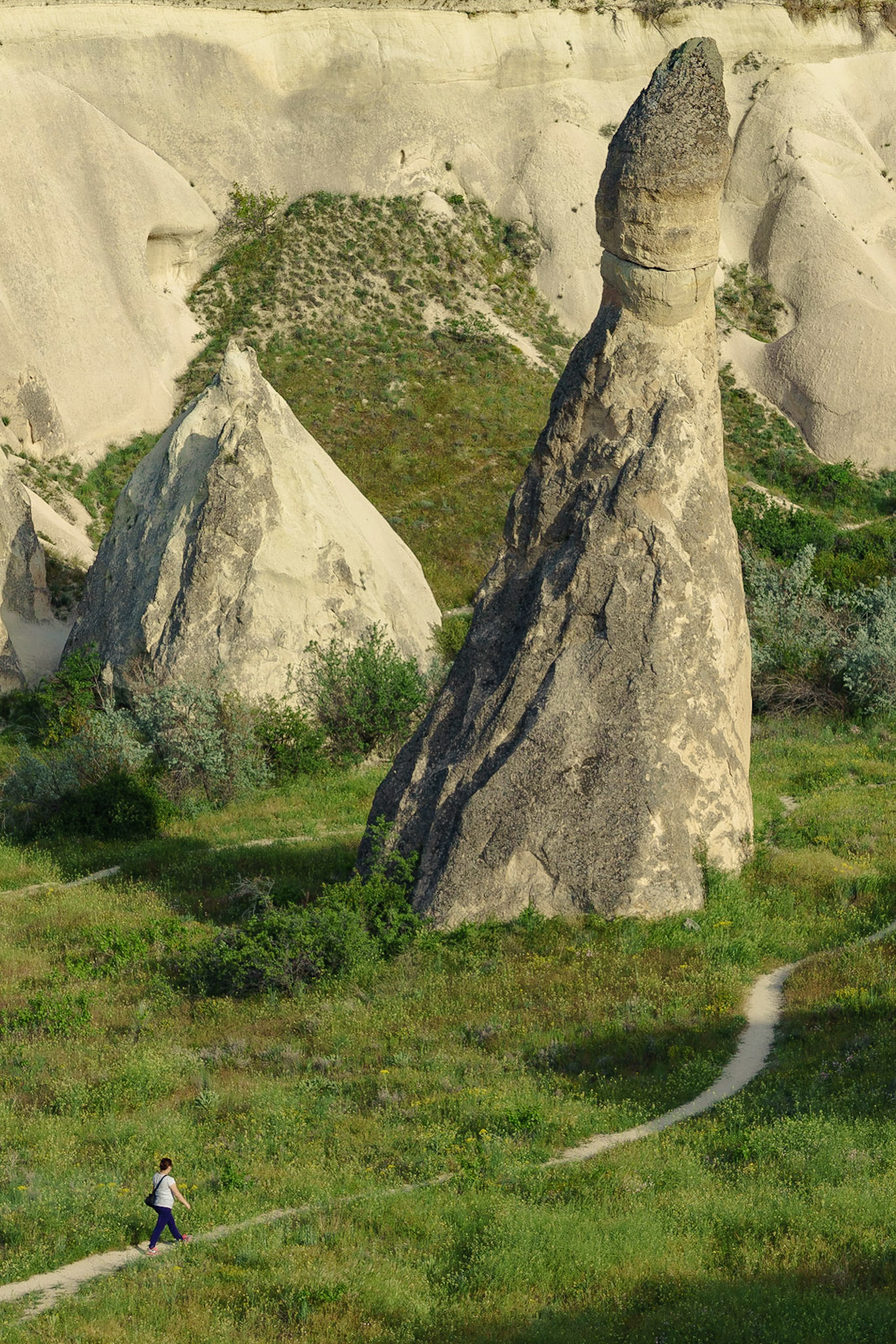Paşabağları'nda tek başına duran bir peribacası ve ona doğru kıvrımlı bir yolda yürüyen kadının uyumlu görüntüsü.