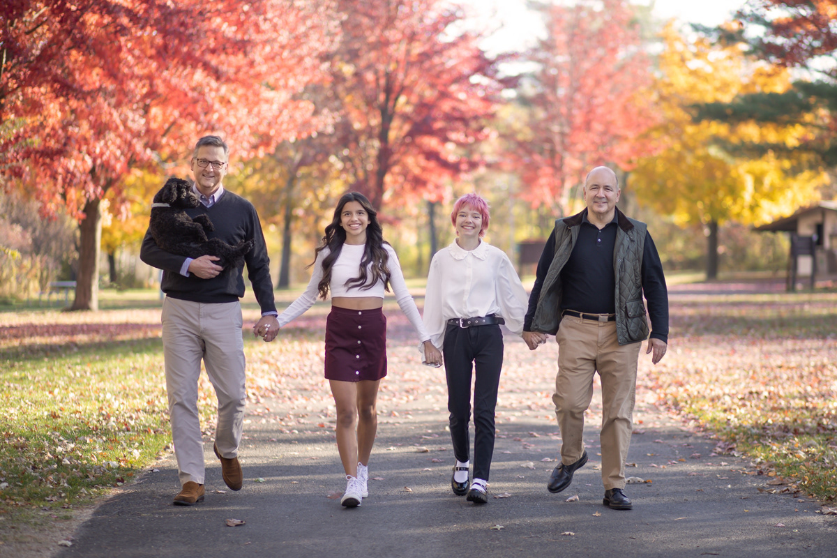 Two men walking down path with their daughters and dog with beautiful fall colors