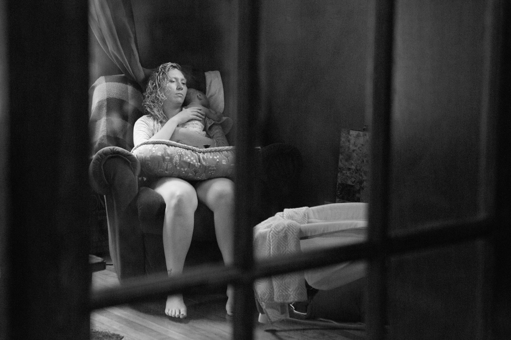 Peering thru glass door at a mom resting her eyes while holder her sleeping baby