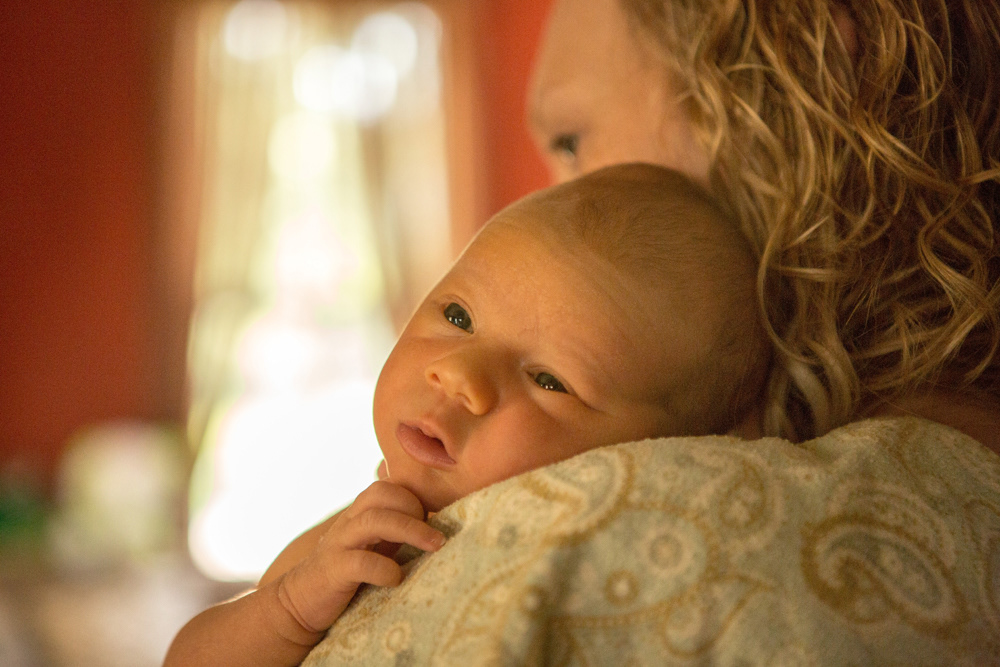 Newborn with eyes open resting on mom's shoulder