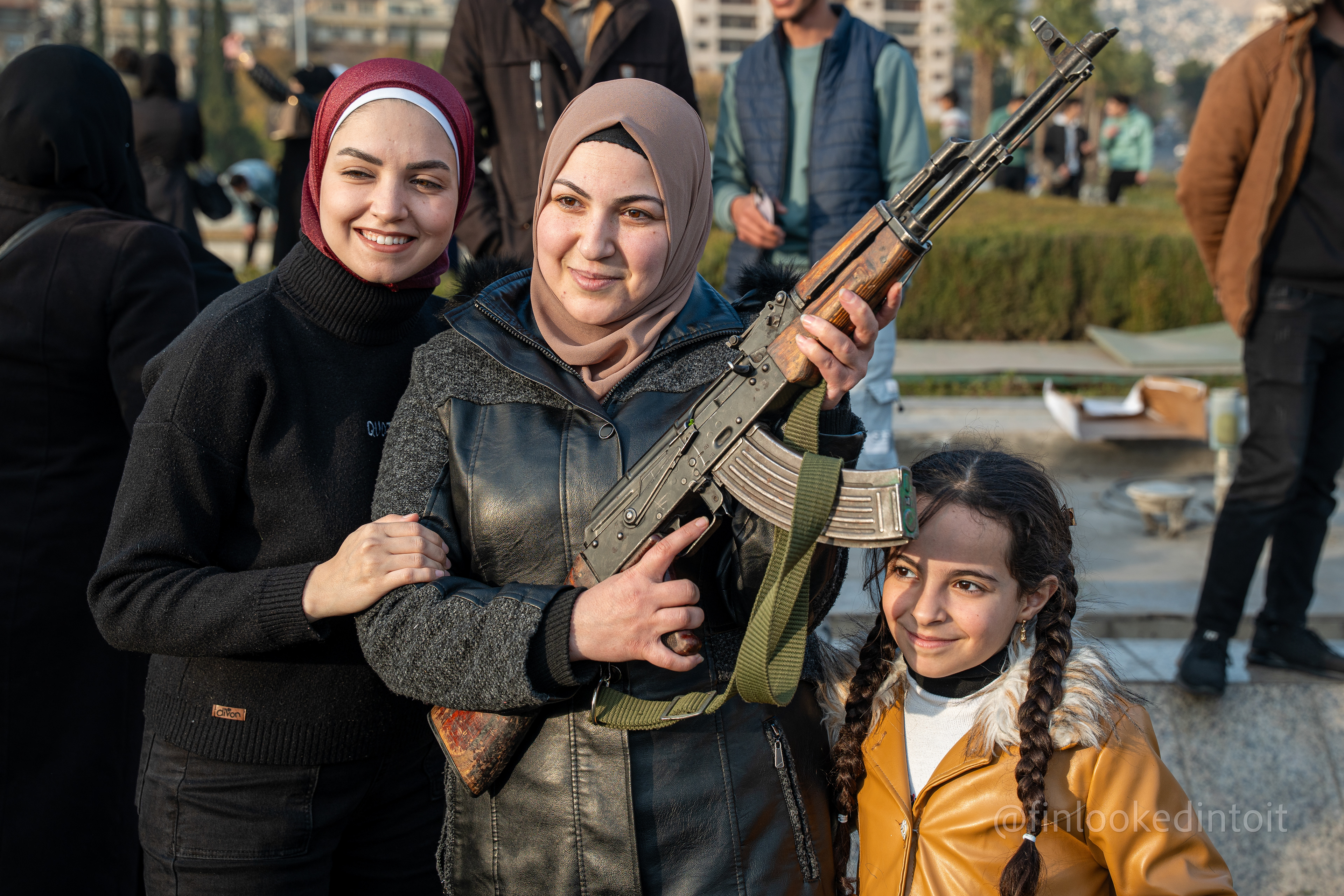 A Syrian mother and her daughters pose with a rebel's rifle in Umayyad Squyare, Damascus, 12/09/2024