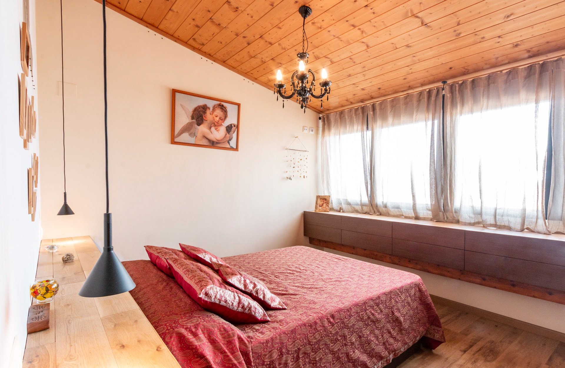 Habitación de matrimonio iluminada por ventanales entre medianeras y techo inclinado recubierto de madera. 