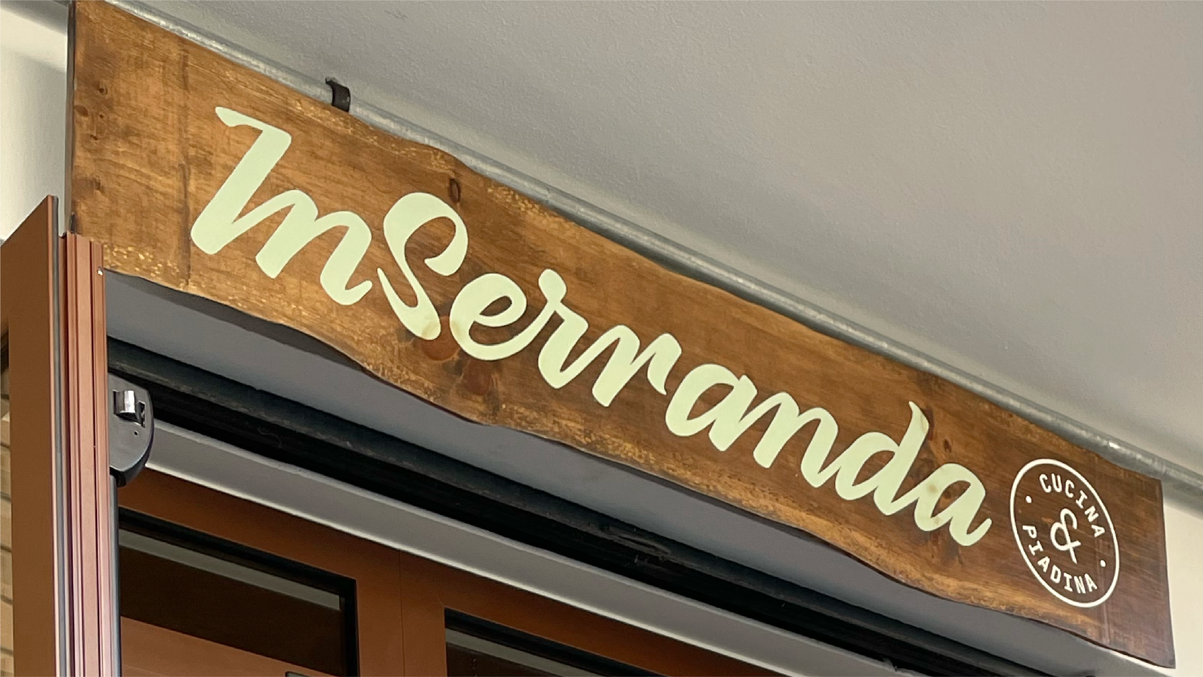 Foto dell'insegna del ristorante InSerranda, dipinta a mano su un legno scuro, la scritta è di verde chiaro.