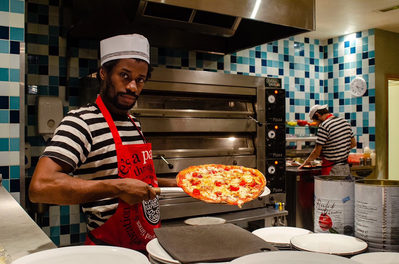Peter, a chef at Pizza Express, presents a pizza just out of the oven while Scott, his co-worker lays the tomato base for the next order in Falmouth, England, December 1, 2018.