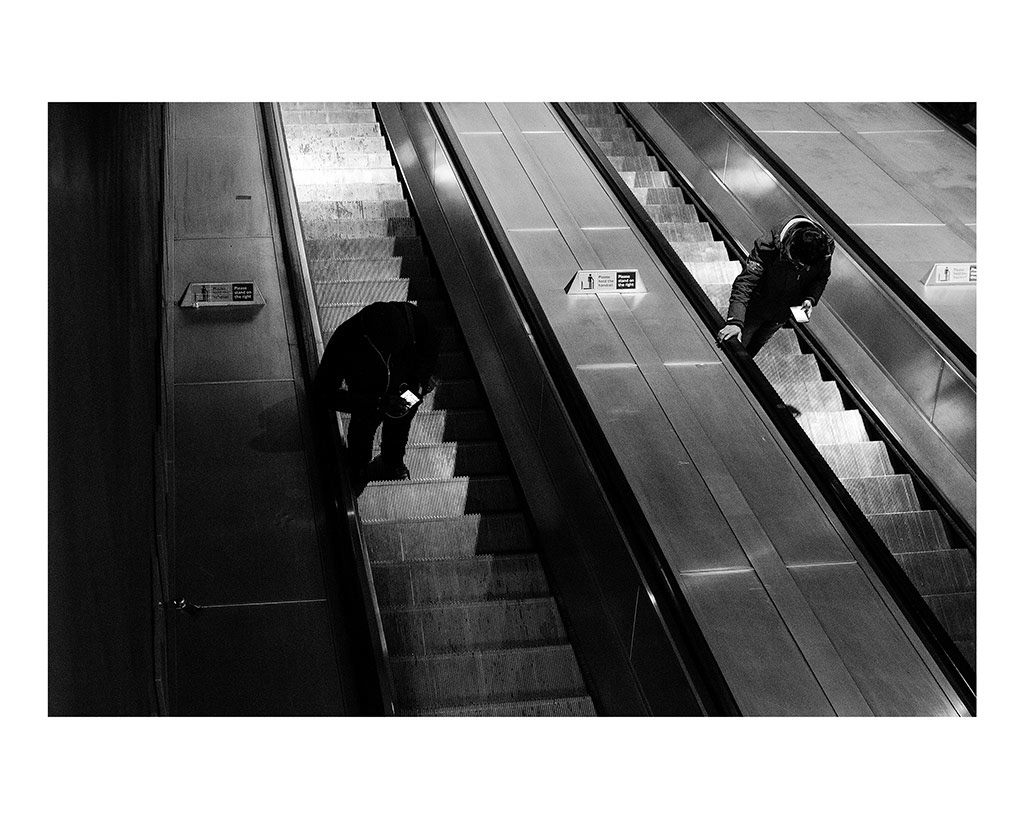 Isolation in London Transport; The City That Never Speaks. 1/5 Two men stand beside each other coming up the escalator, looking down at their phones, oblivious to one another in the London Underground, England, November 26, 2018.