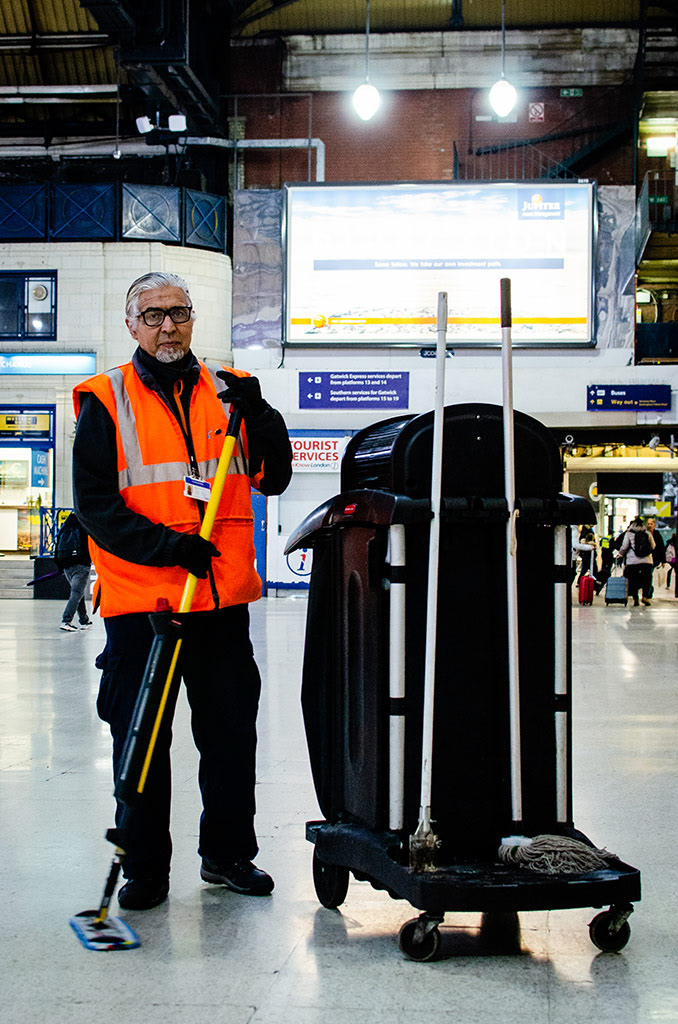 Bachir, a cleaner working for Network Rail in Victoria Station, mops the floor standing next to his trolley, in front of signs that dominate the station in London, England, November 24, 2018. 