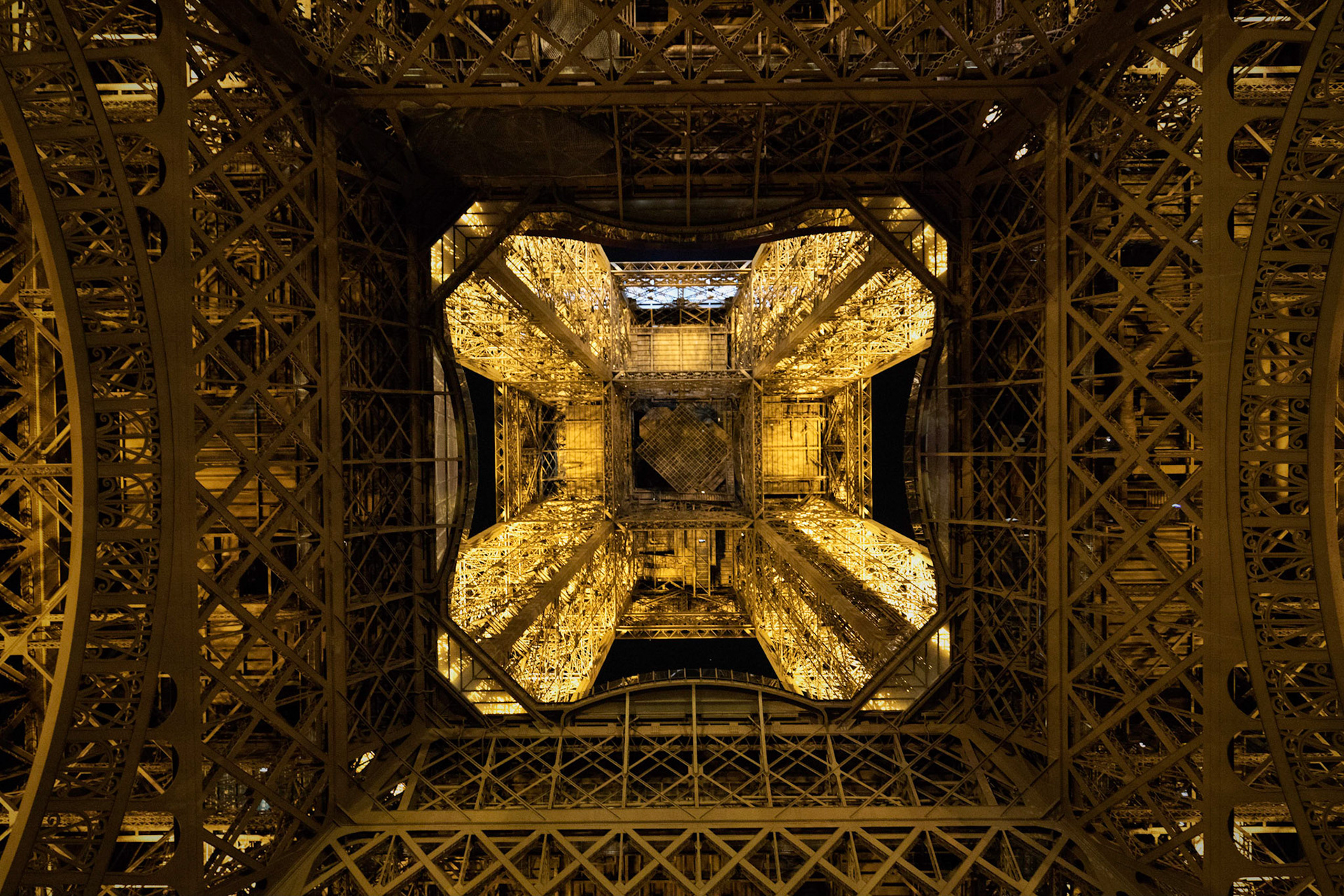 A photo taken from directly beneath the Eiffel Tower and pointed upward. This showcases the iron work of the structure.