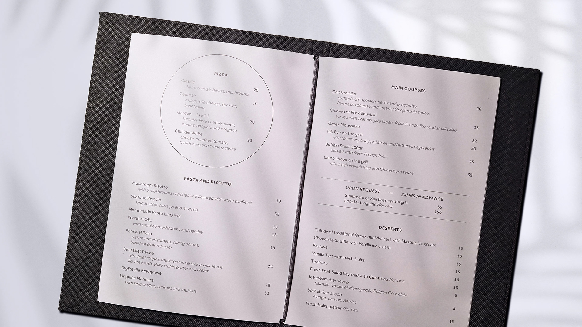 IKIES Santorini boutique hotel menu design, opened, showcasing the layout. The image is taken in the shadow of a plant.