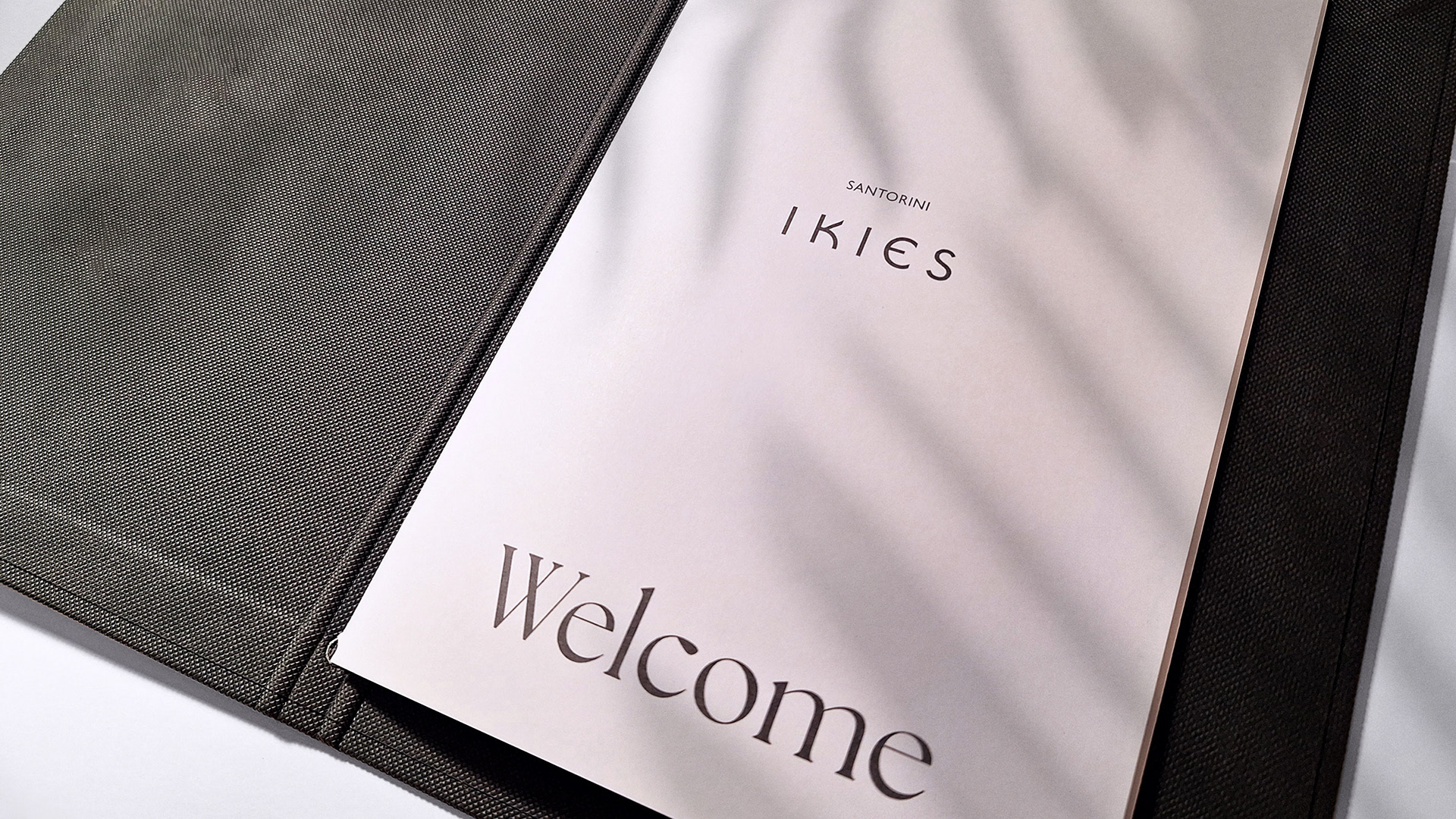 IKIES Santorini boutique hotel menu design opened at the first page, welcoming the guests. The image is taken in the shadow of a plant.