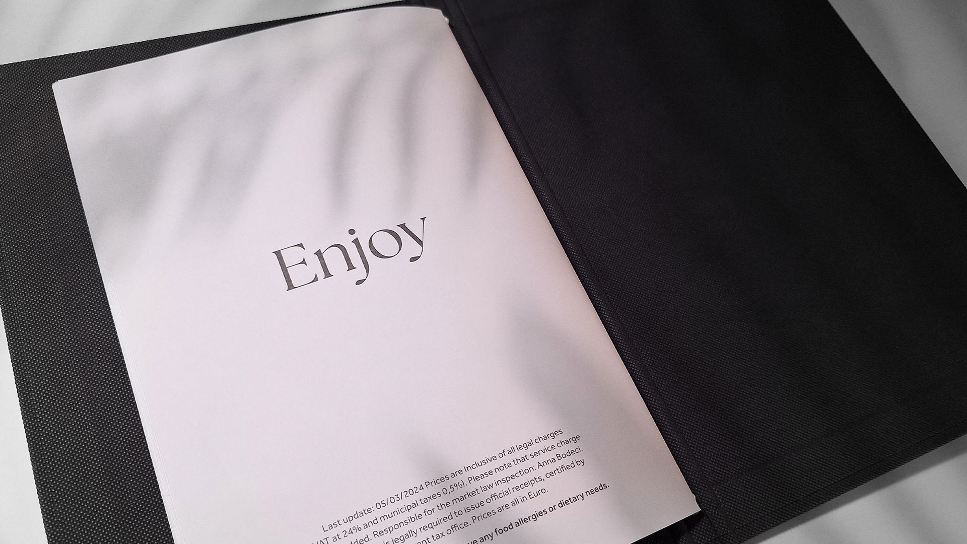 IKIES Santorini boutique hotel menu design opened at the final page, calling the guests to enjoy their meal. The image is taken in the shadow of a plant.