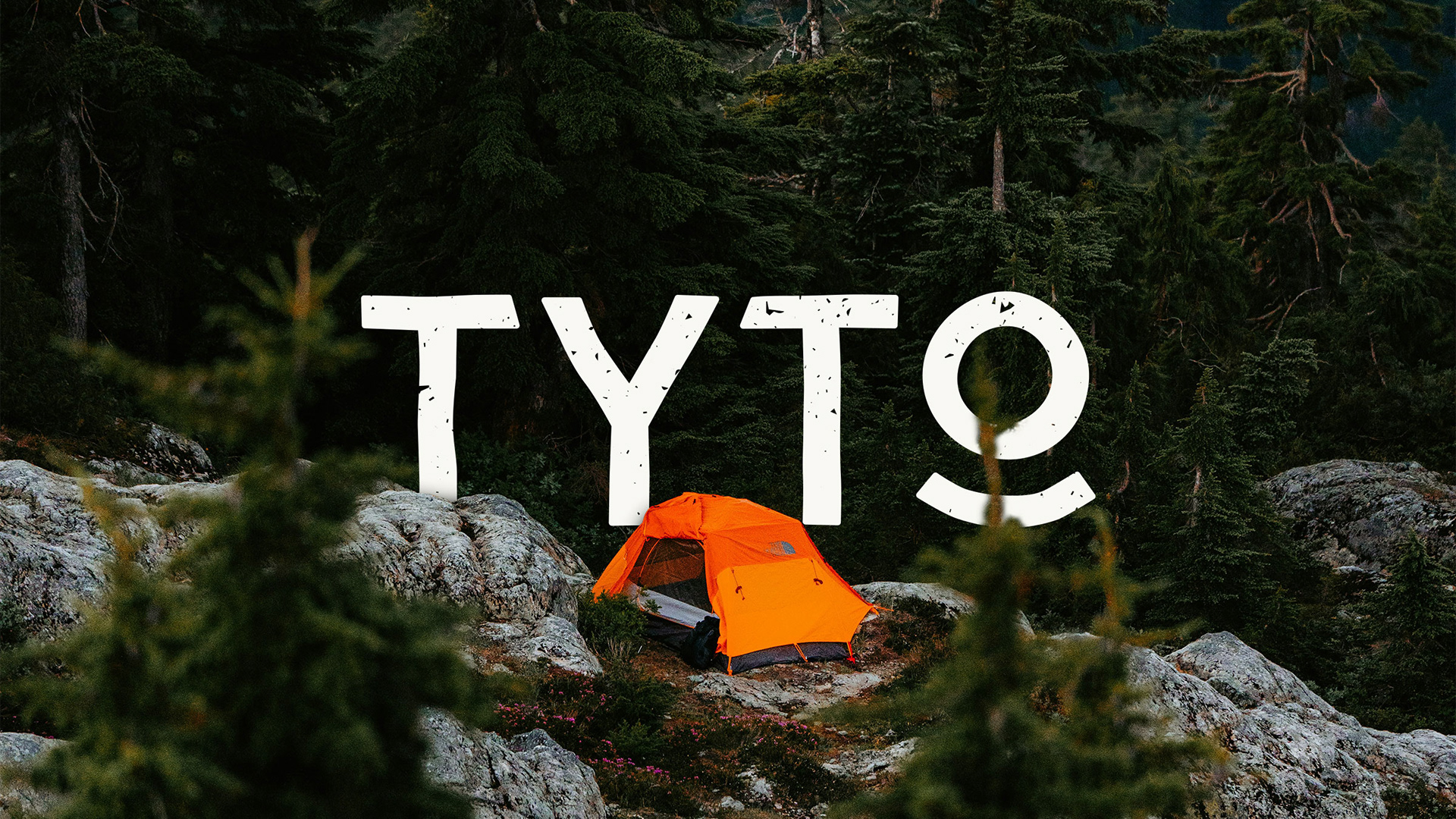The TYTO hiking logotype in warm white, placed in a photo of an orange tent in the forest. Elements of the photo like rocks and trees overlap with the logo, as to seem placed in the scene.