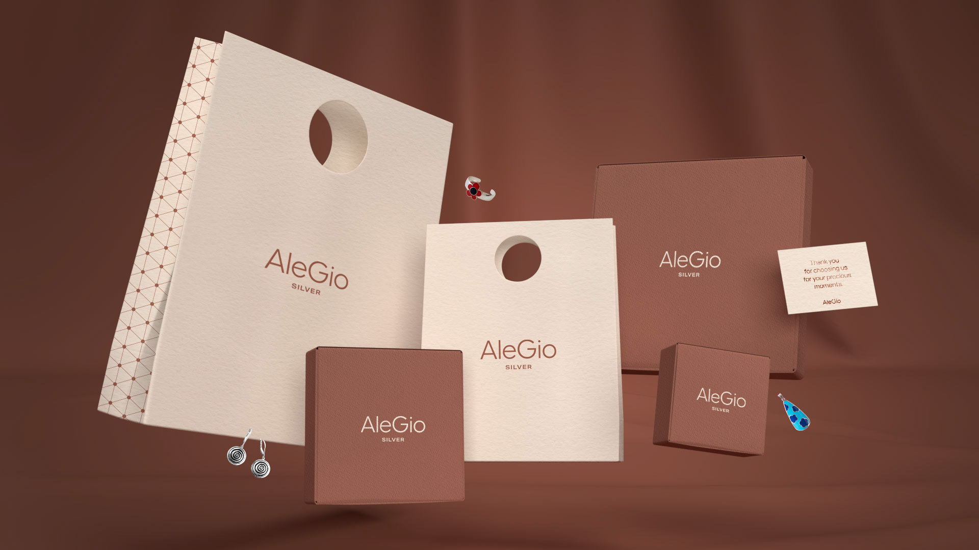 AleGio silver jewelry bags and boxes in the brand colors and featuring the company's logotype. All items are flying and around them are silver jewels, also in the air.