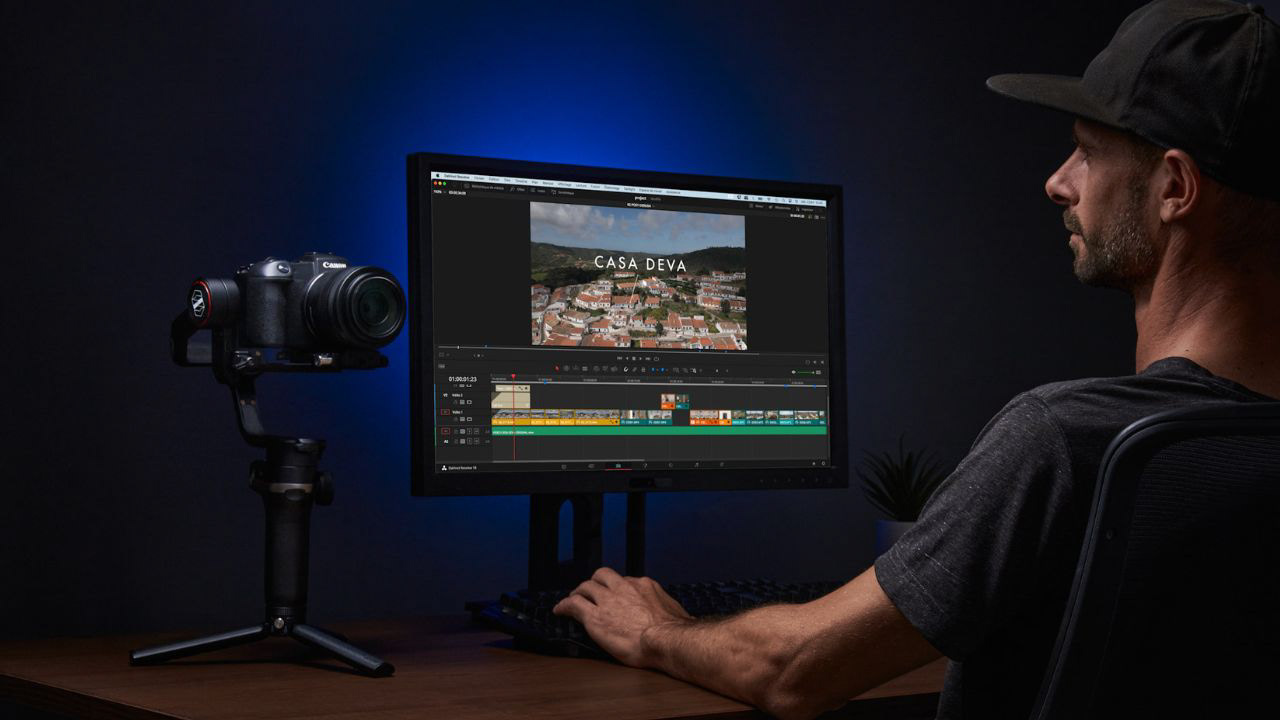 Photograph of a real estate videographer editing a video on a large screen with a professional camera and gimbal nearby
