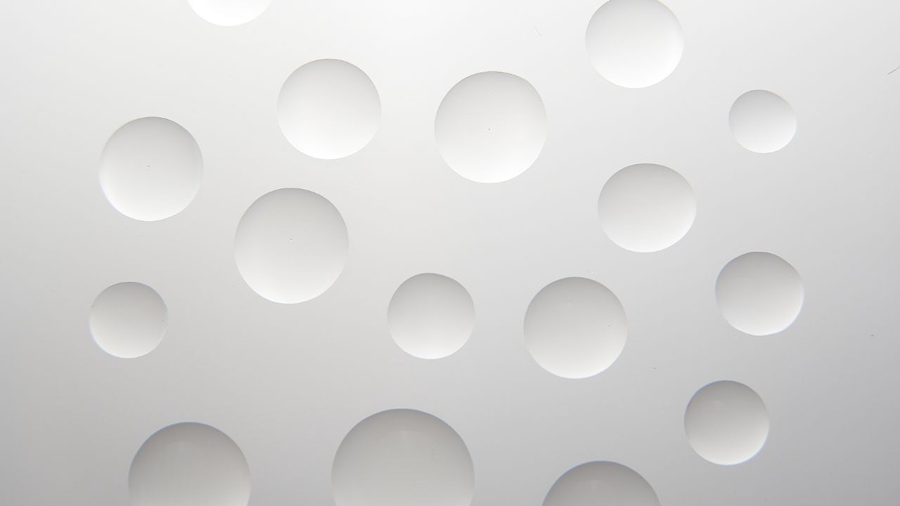 Clean, minimalist commercial photography of a white textured surface with embossed, glossy circles, highlighting abstract design and light reflection