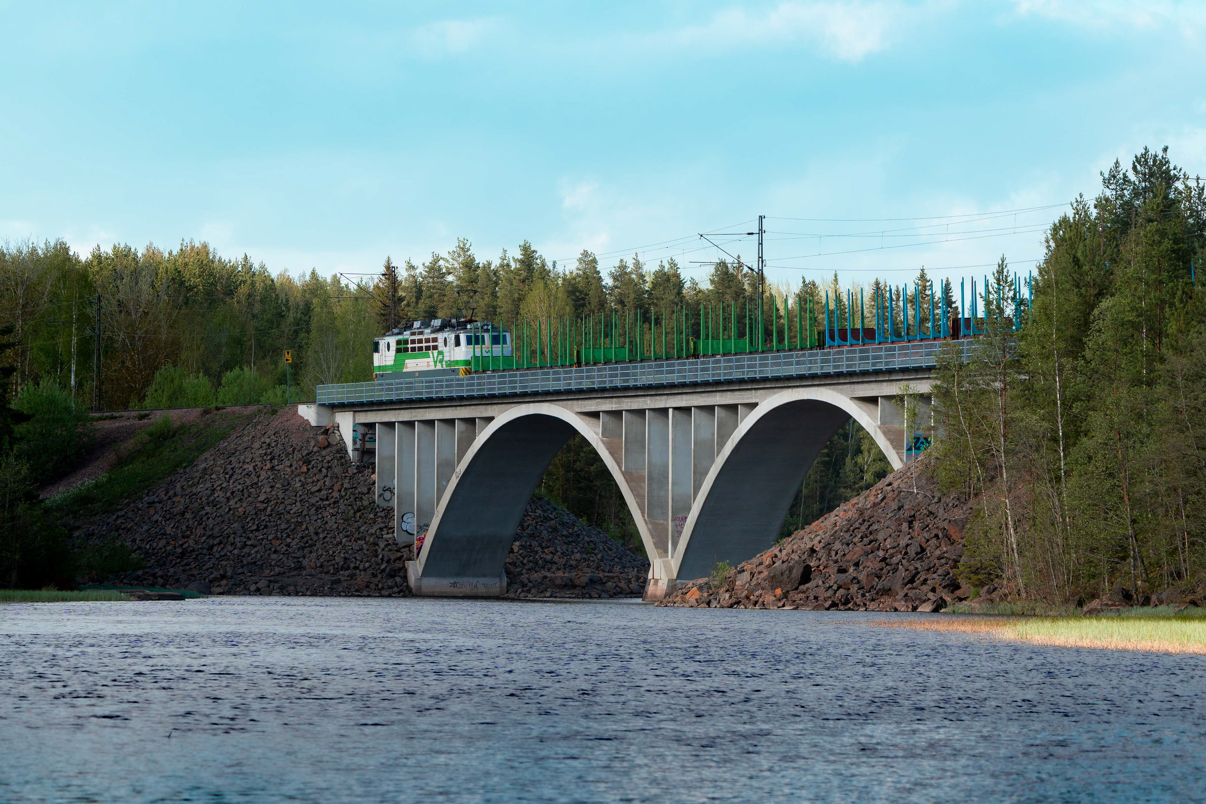 Sr-1-sähköveturi ylittämässä Harjunsalmen siltaa matkalla Kouvolan lajittelusta Iisalmeen tyhjien tukkivaunujen kanssa. (25.5.2025)