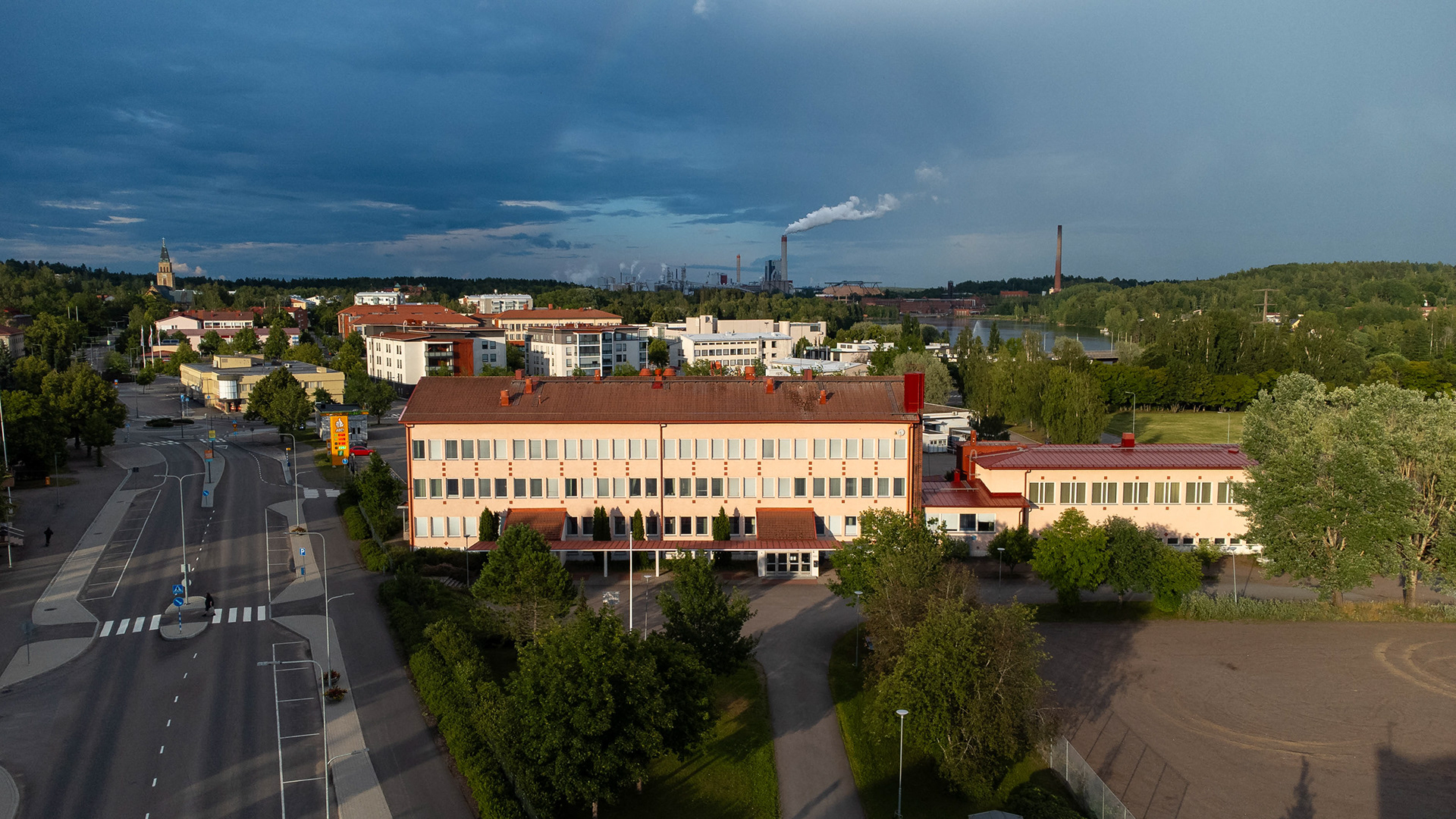 Kuusankosken lukio kesäauringon paisteessa. Taustalla Kuusankosken keskustaa sekä UPM Kymin tehdas. (8.7.2023)
