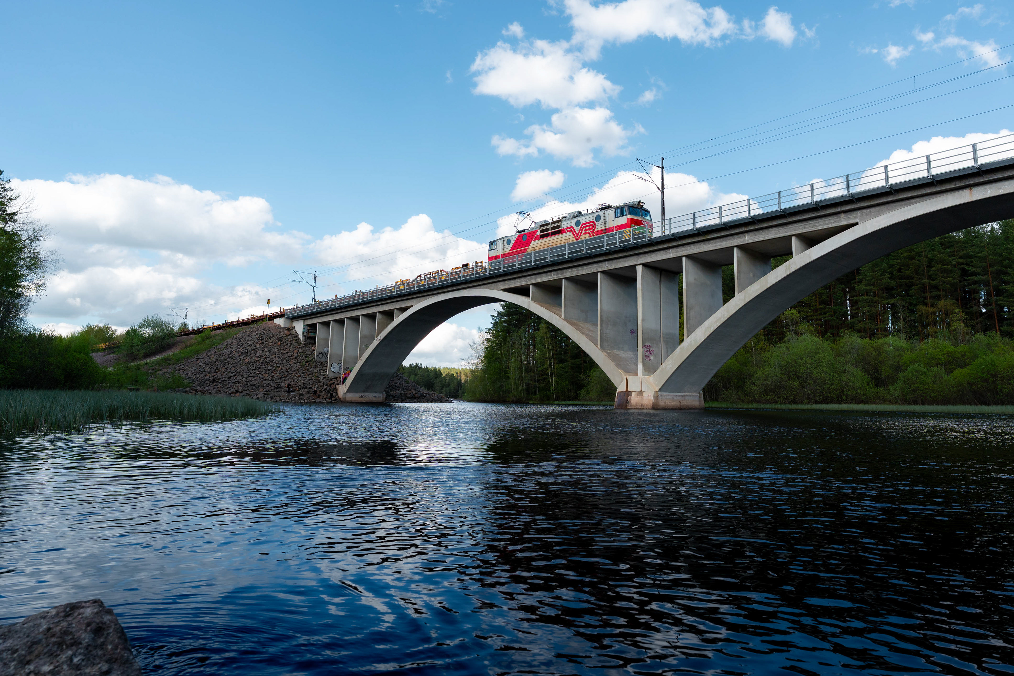 Sr-1-sähköveturi siirtämässä tyhjiä kiskonkuljetusvaunuja Hankasalmelta Kouvolan lajitteluun Harjunsalmen sillalla. (25.5.2025)