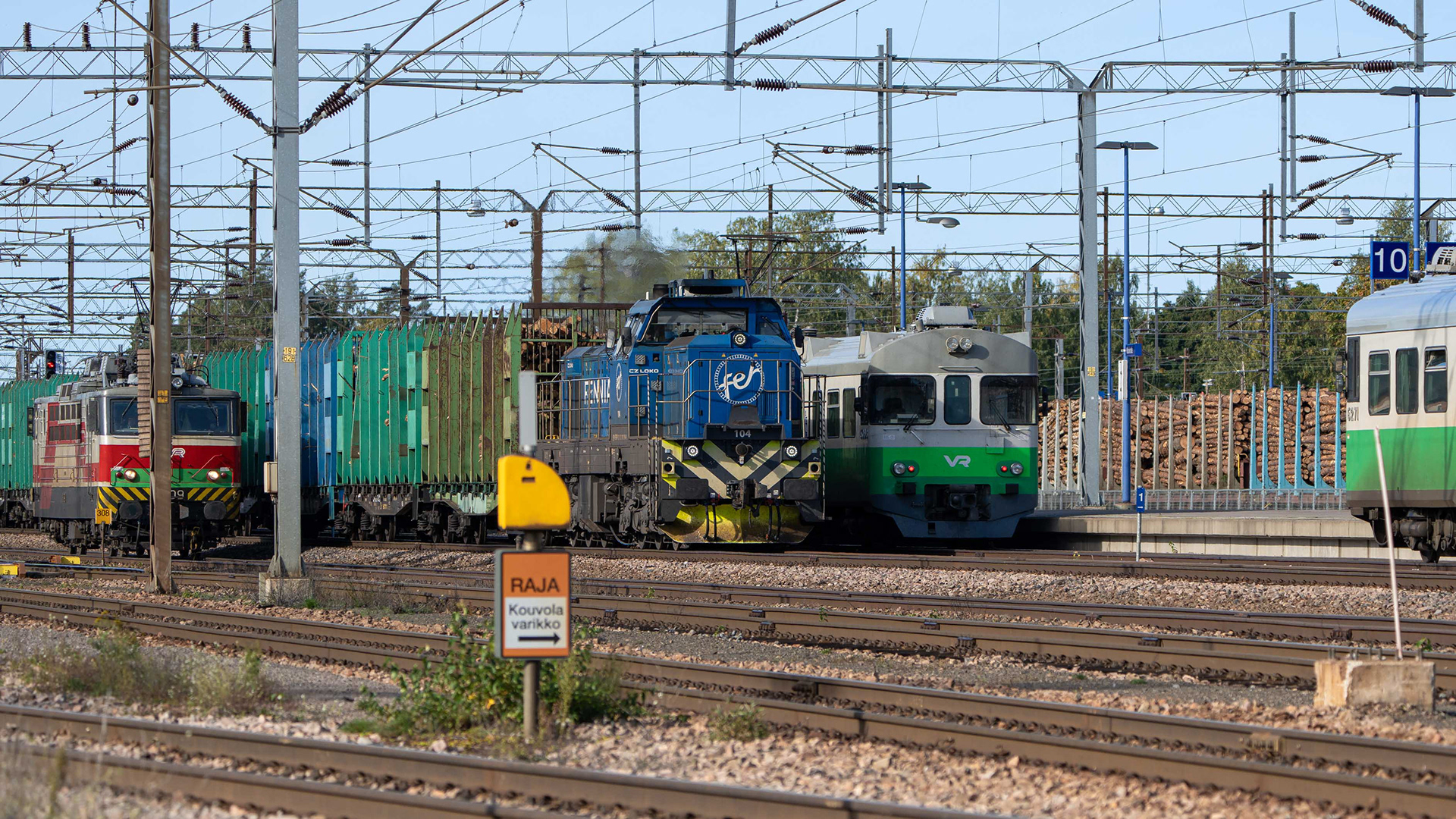 Toijalasta lähtenyt Fenniarail Oy:n Dr18-dieselveturin vetämä tukkijuna ohittaa Kouvolan aseman. Vieressä parkissa Sr-1 sähköveturi sekä Sm2 -sähkömoottorijuna. (22.9.2024)