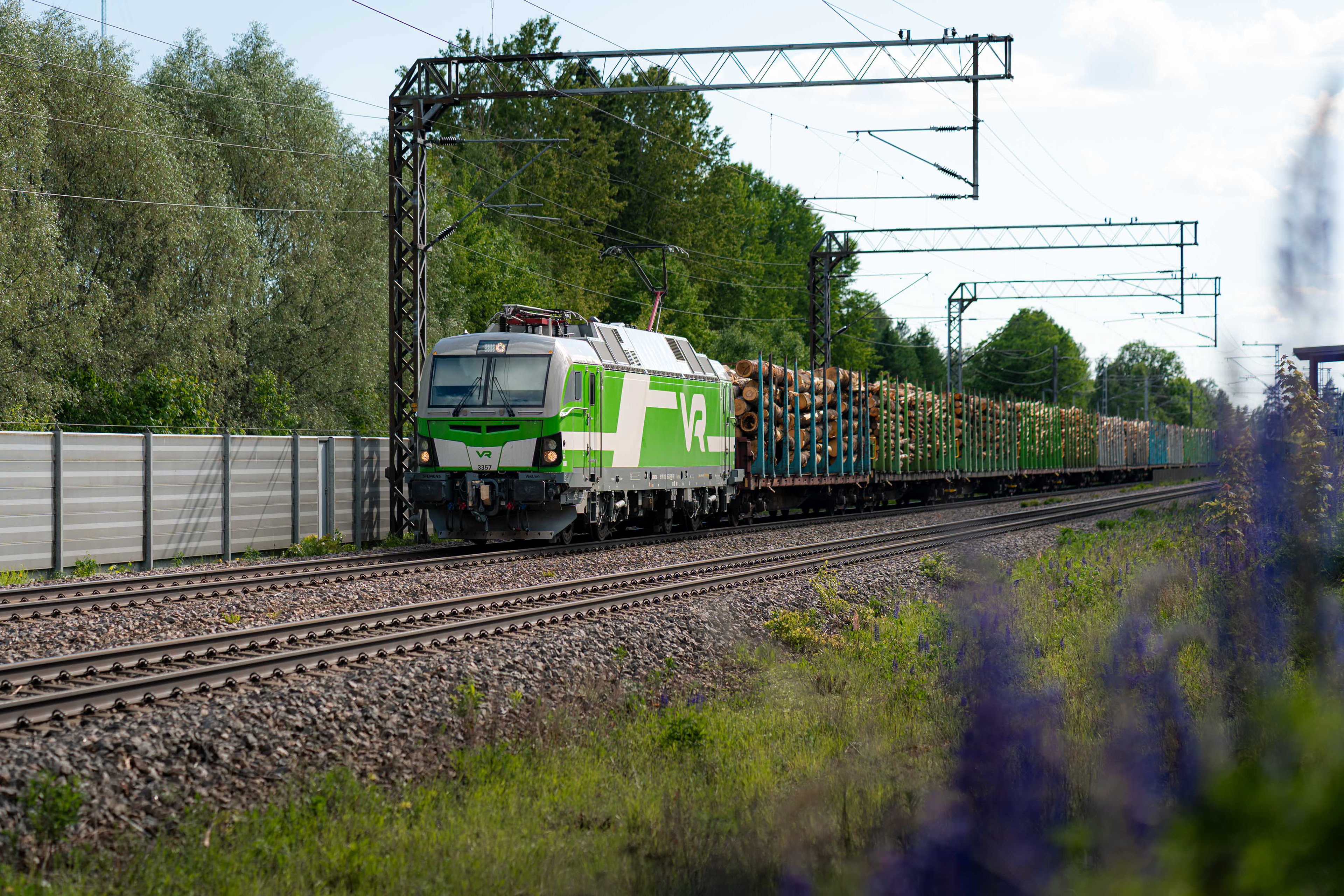 Sr3-sähköveturin vetämä tukkijuna ohittaa Korian aseman matkallaan Akaan raakapuuterminaalista Kouvolan lajitteluun. (3.6.2026)