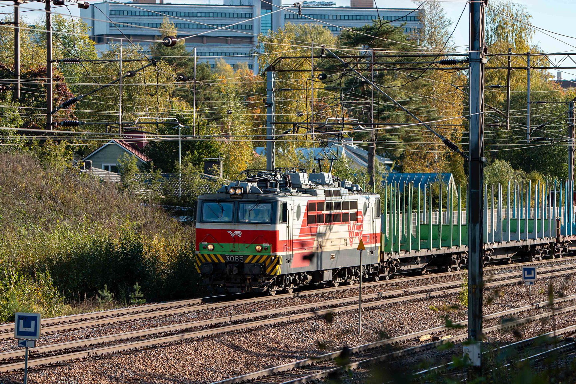 Sr1-veturi kuljettamassa tyhjiä raakapuuvaunuja Kouvolan ratapihalta Pieksämäen ratapihalle. Kuvan taustalla näkyy Kouvolan keskustaajamaa ja Pohjolatalo. (22.9.2024)