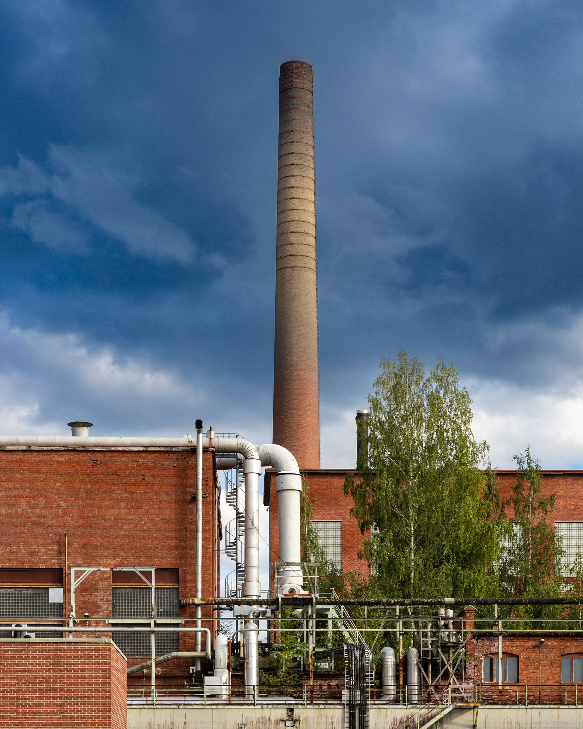 Kymintehtaan vanhoja tehdasrakennuksia ja taustalla höyryvoimalaitoksen piippu. (8.2023)