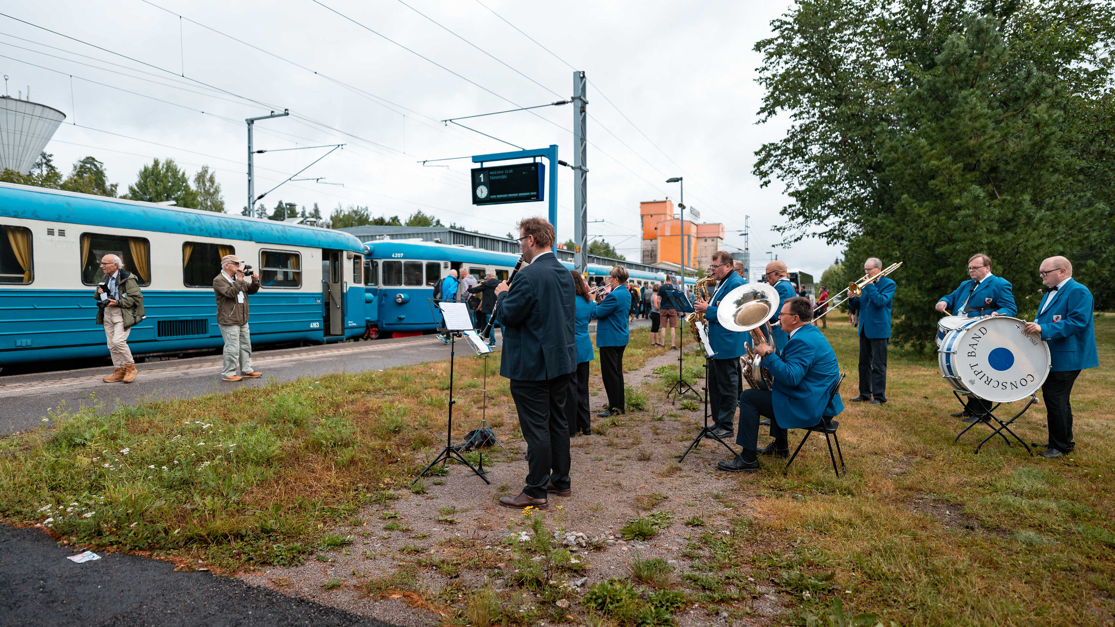 Elimäen puhallinorkesteri soittamassa Korian aseman edustalla lättähatun saapuessa Korian rautatiesillan 100-vuotisjuhlapäivänä. (2.8.2025)