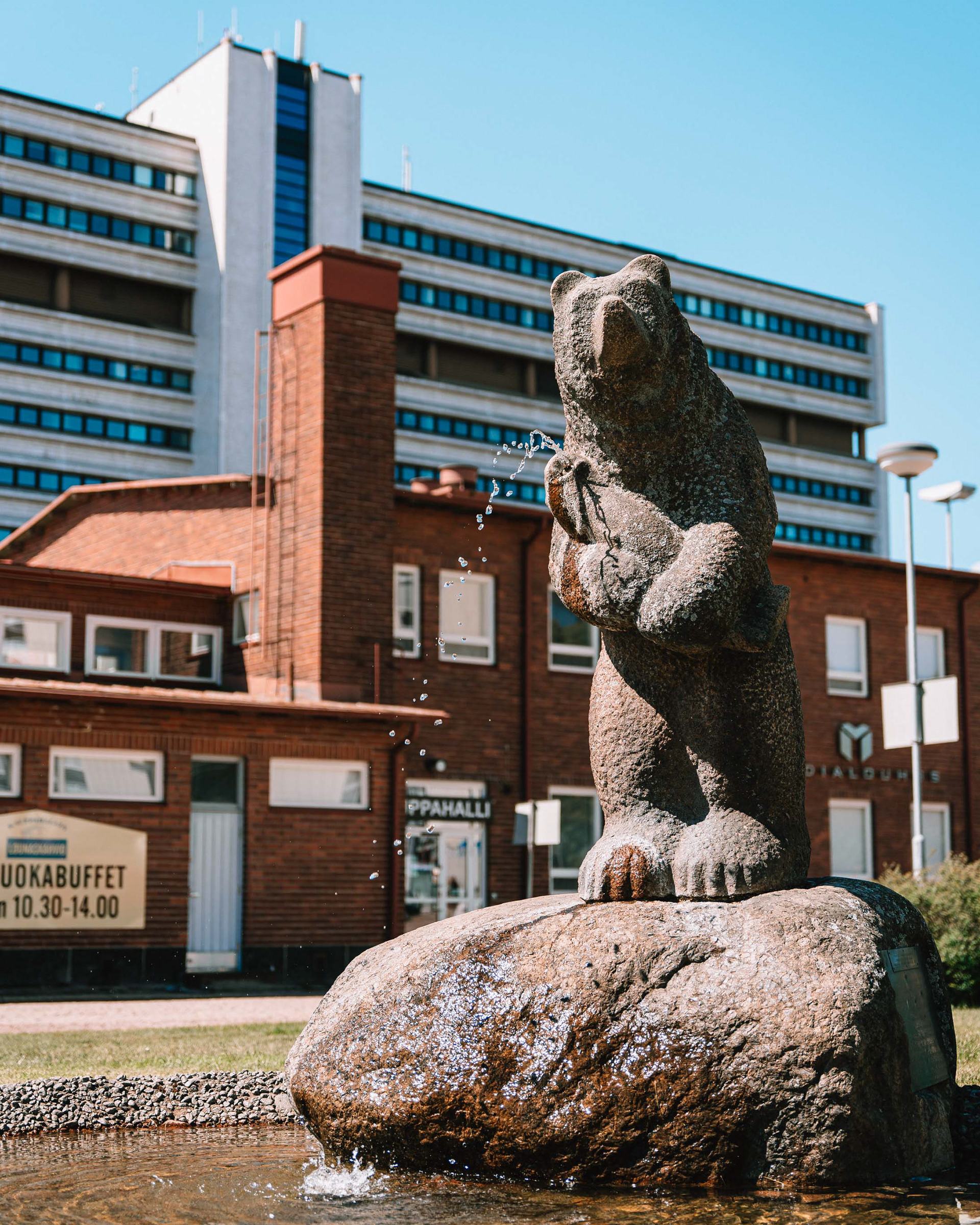 Kalastava karhu patsas Kauppahallin edustalla. Taustalla Pohjolatalo.