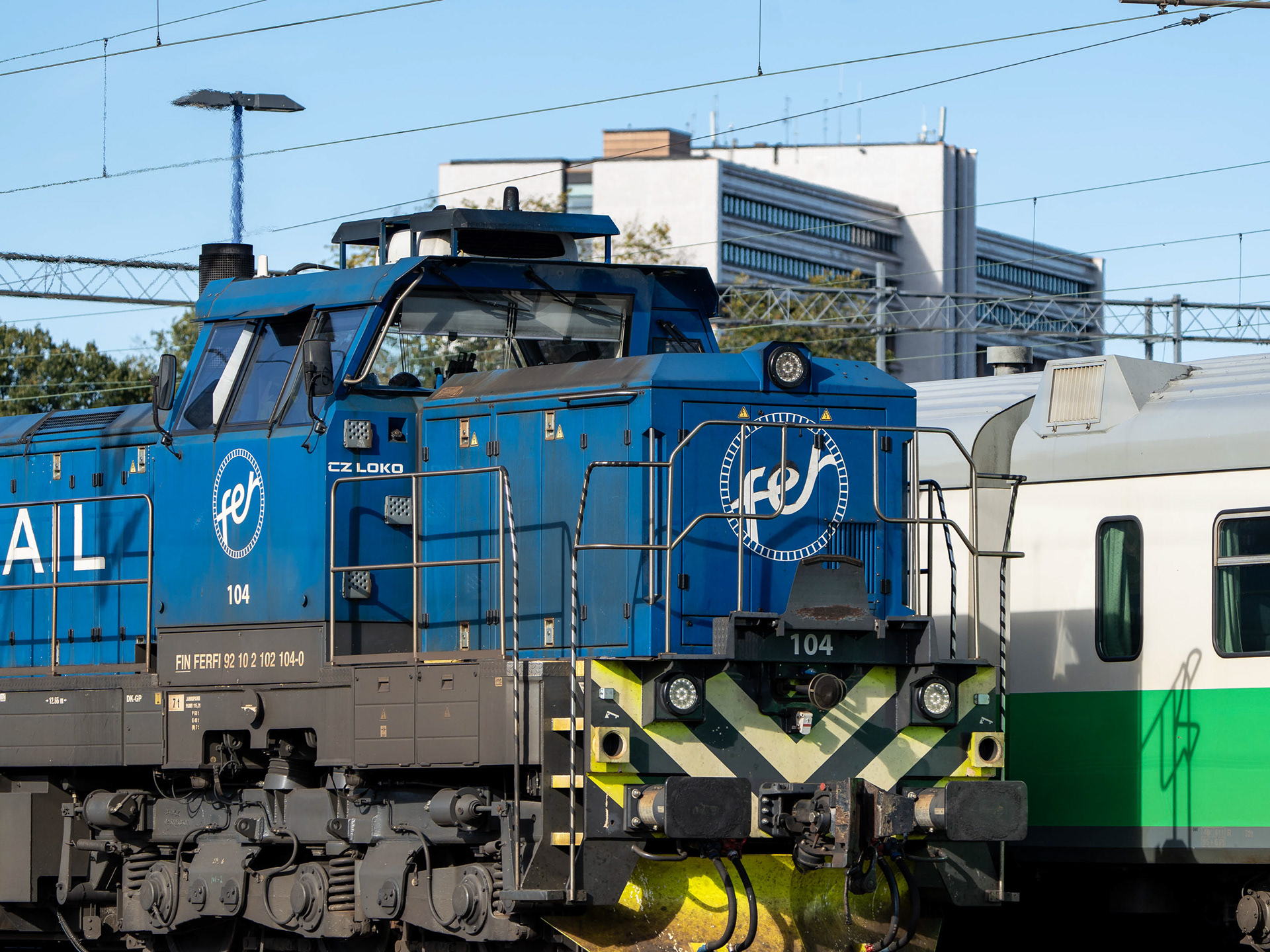 Fenniarailin Dr-18-dieselveturi Kouvolan asemalla. Viereisellä raiteella Sm2-juna ja taustalla Kouvolan keskustassa sijaitseva Pohjola-talo (22.9.2024)
