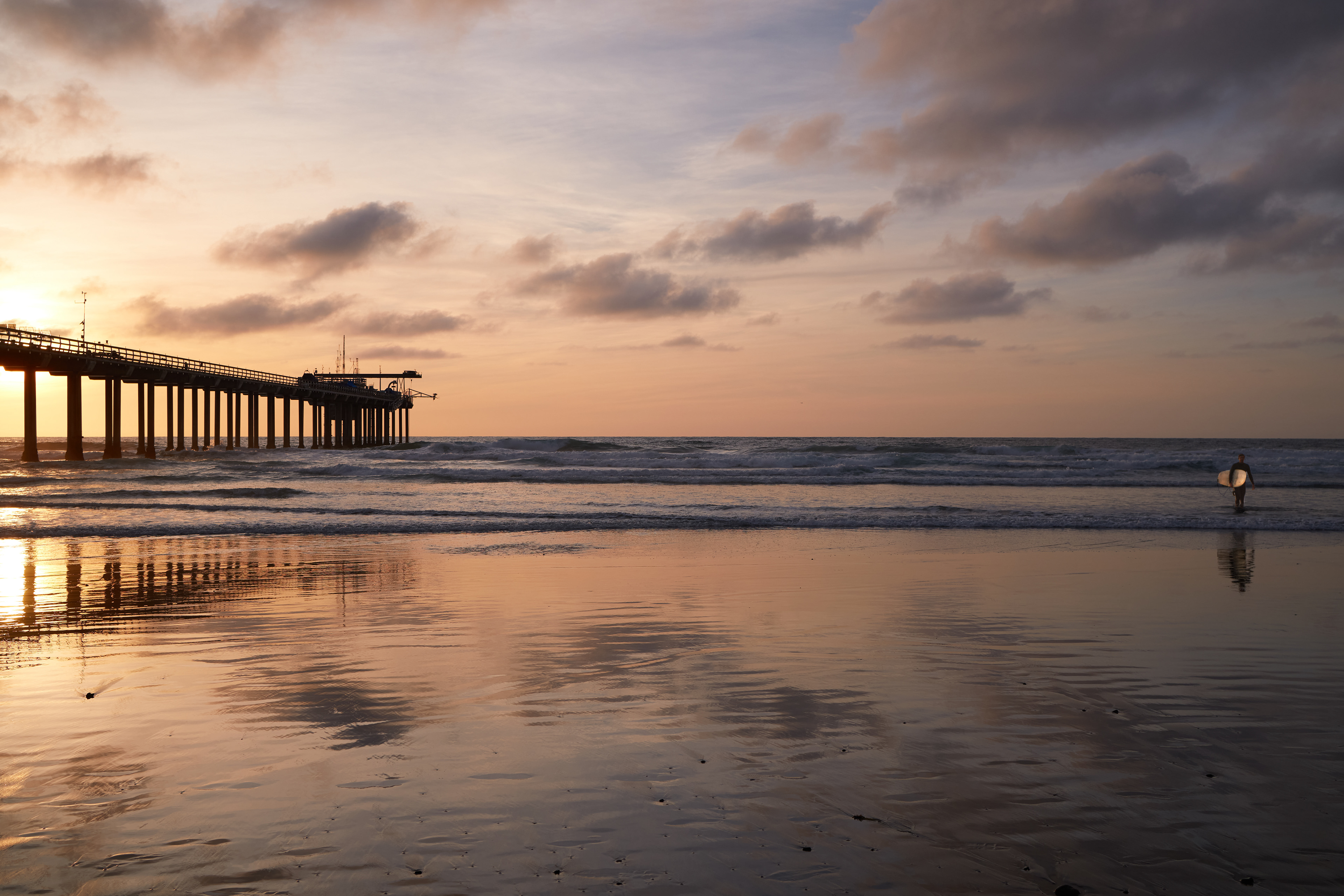 Photograph of a surfer walking out of the surf during sunset near the Scripps Pier